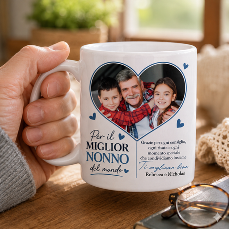 Tazza bianca con foto in cuore blu e dedica, afferrata con la mano.