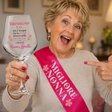 Fascia rosa “Migliore Nonna” con fiori e calice da vino con dedica; donna festeggia